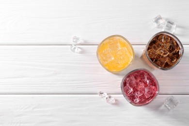 Photo of Soda water of different flavors in glasses with ice cubes on white wooden table, top view. Space for text