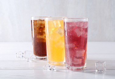 Photo of Soda water of different flavors in glasses with ice cubes on white wooden table