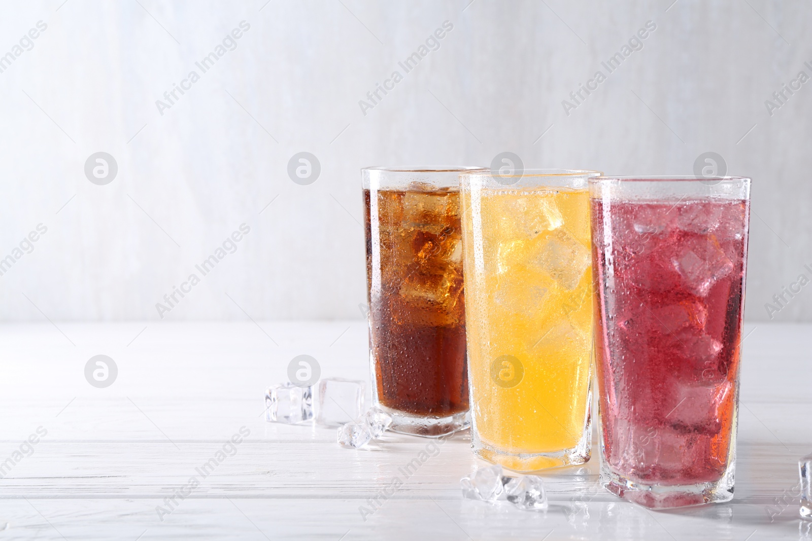 Photo of Soda water of different flavors in glasses with ice cubes on white wooden table, space for text