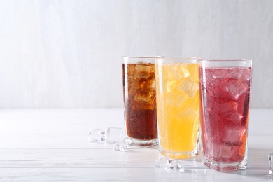 Photo of Soda water of different flavors in glasses with ice cubes on white wooden table, space for text