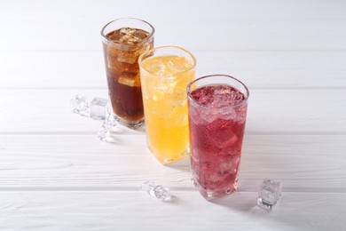 Photo of Soda water of different flavors in glasses with ice cubes on white wooden table