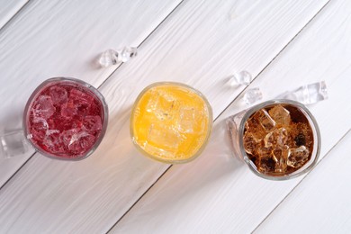 Photo of Soda water of different flavors in glasses with ice cubes on white wooden table, top view