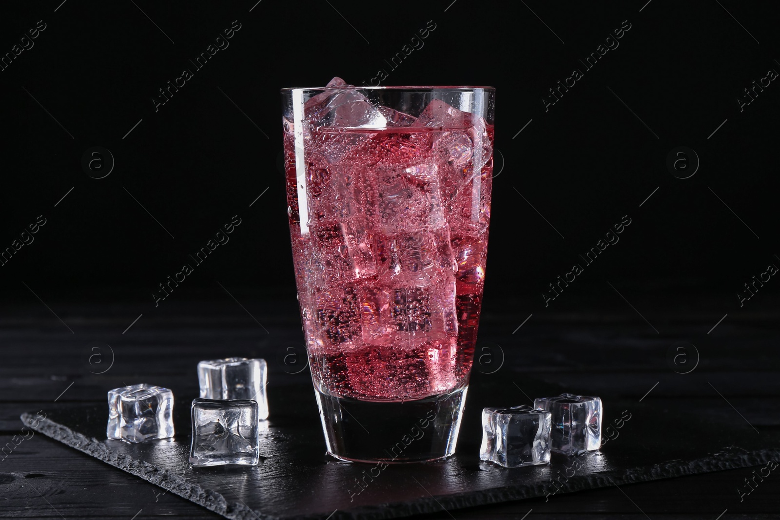 Photo of Sweet soda water in glass with ice cubes on black wooden table