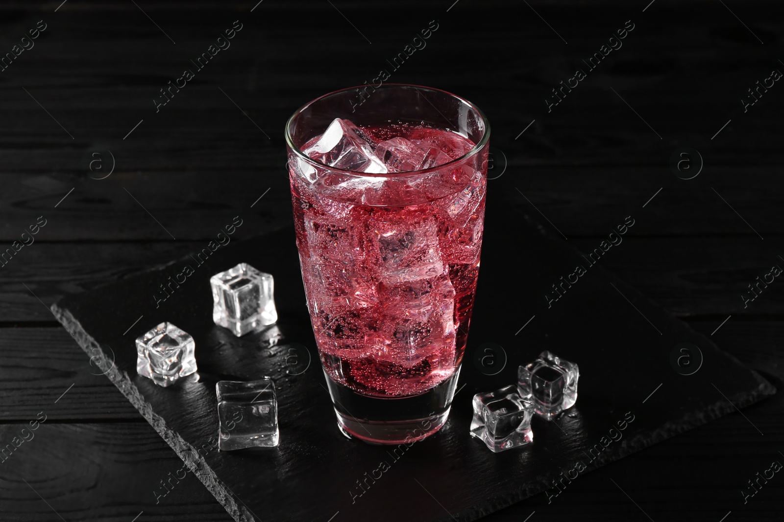 Photo of Sweet soda water in glass with ice cubes on black wooden table