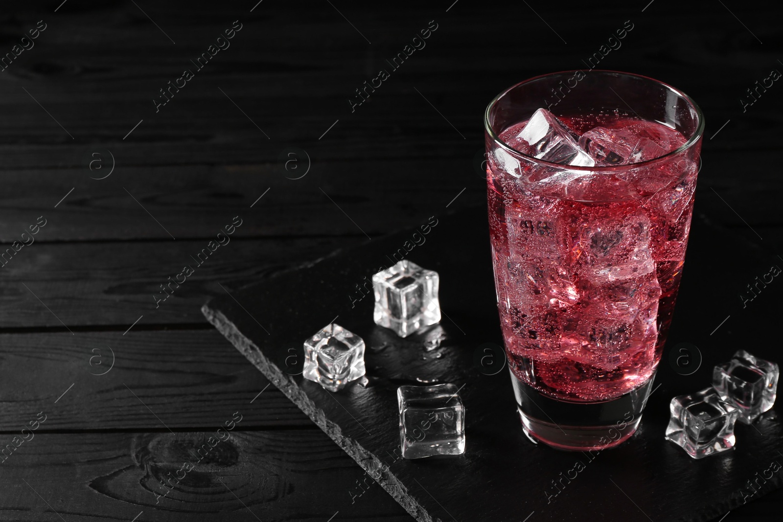 Photo of Sweet soda water in glass with ice cubes on black wooden table, space for text