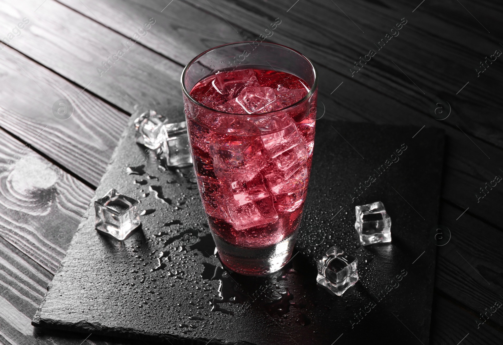 Photo of Sweet soda water in glass with ice cubes on black wooden table