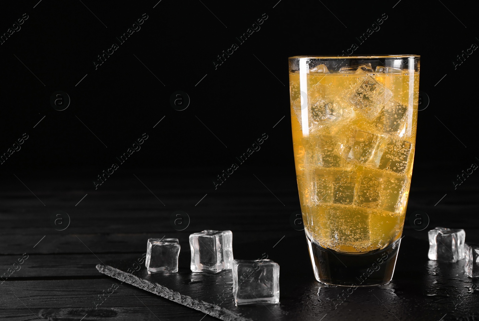 Photo of Sweet soda water in glass with ice cubes on black wooden table, space for text