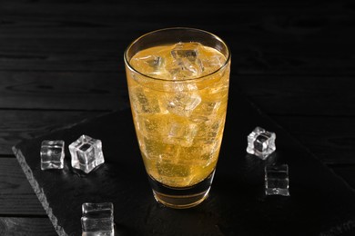 Photo of Sweet soda water in glass with ice cubes on black wooden table