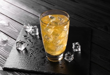 Photo of Sweet soda water in glass with ice cubes on black wooden table