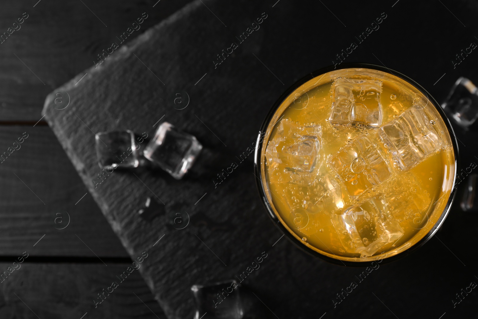 Photo of Sweet soda water with ice cubes in glass on black wooden table, top view. Space for text