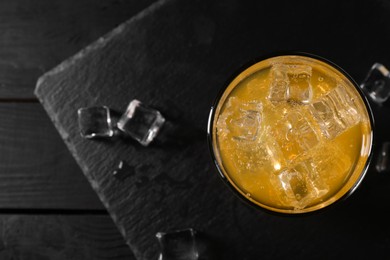 Photo of Sweet soda water with ice cubes in glass on black wooden table, top view. Space for text