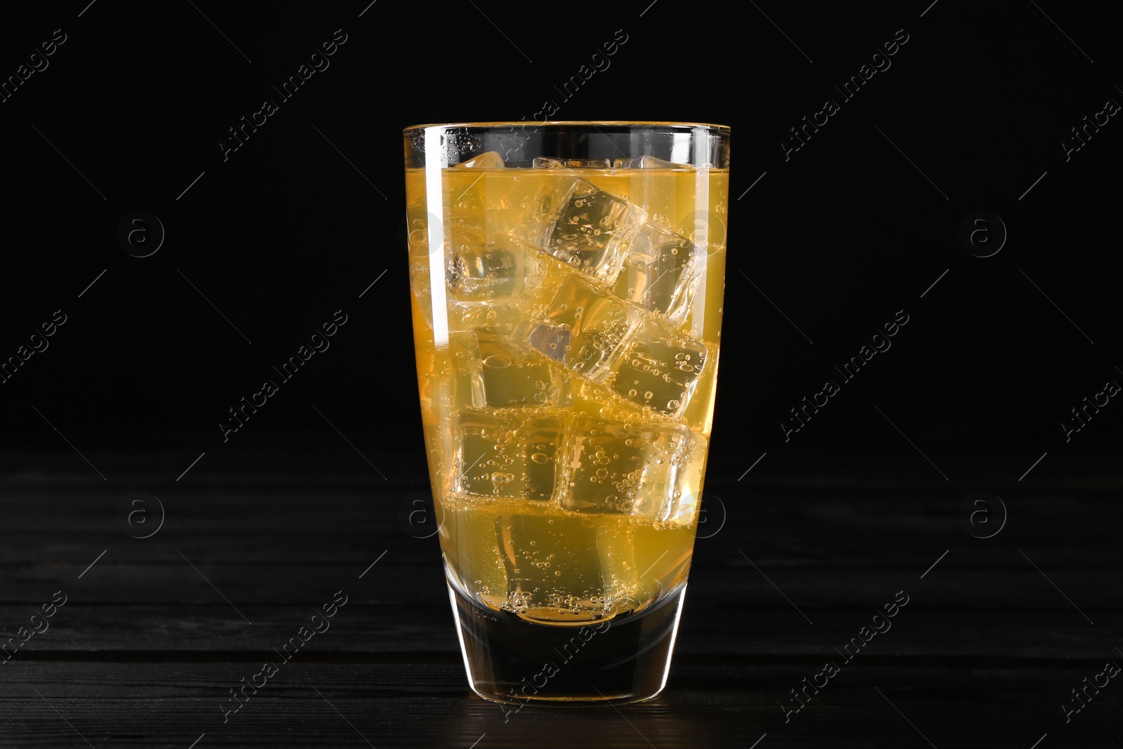 Photo of Sweet soda water with ice cubes in glass on black wooden table