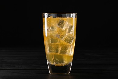 Photo of Sweet soda water with ice cubes in glass on black wooden table