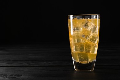 Photo of Sweet soda water with ice cubes in glass on black wooden table, space for text