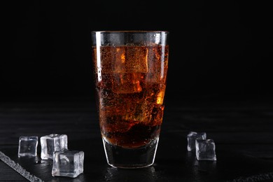 Photo of Sweet soda water in glass with ice cubes on black wooden table