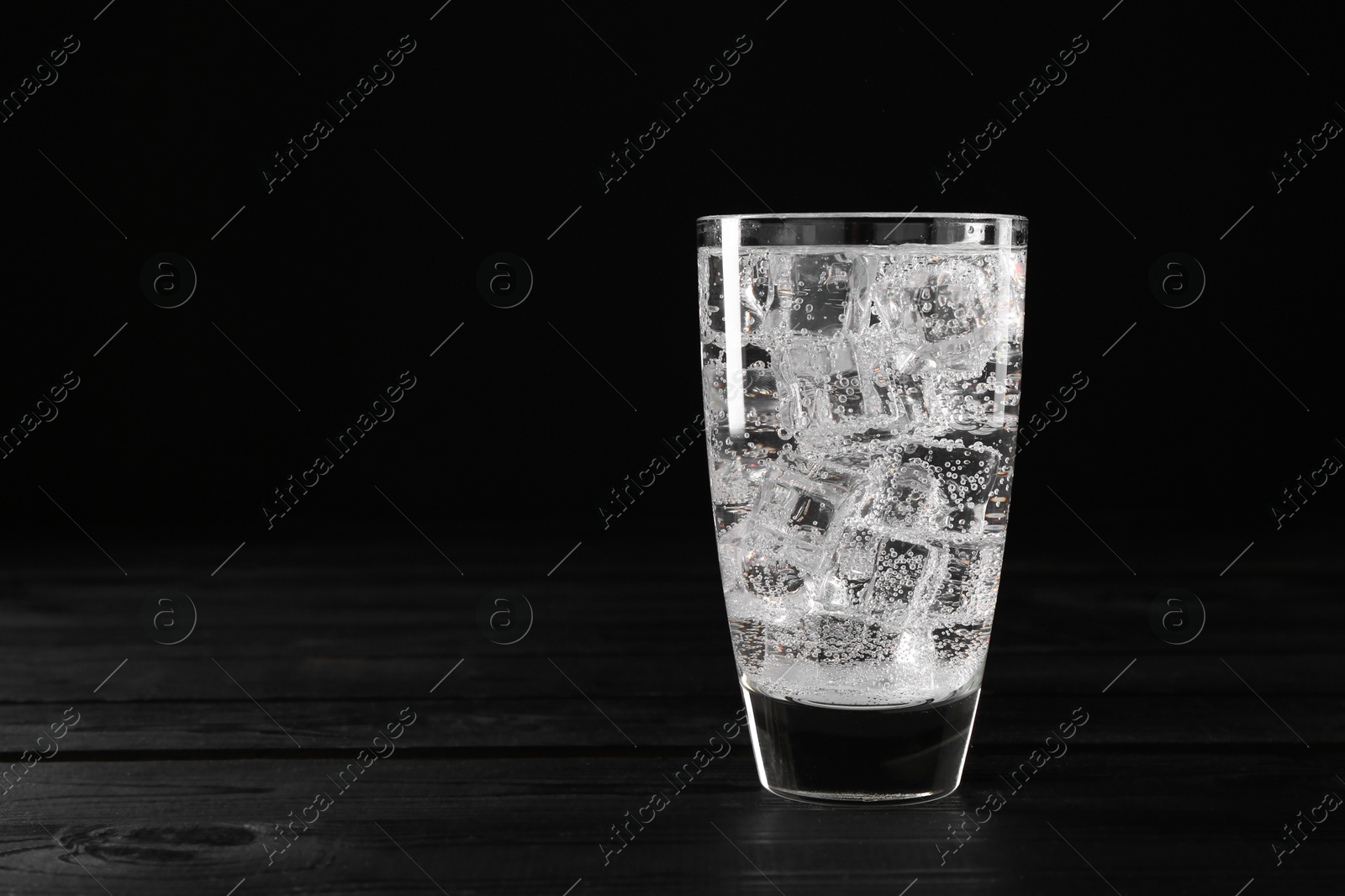 Photo of Refreshing soda water with ice cubes in glass on black wooden table, space for text