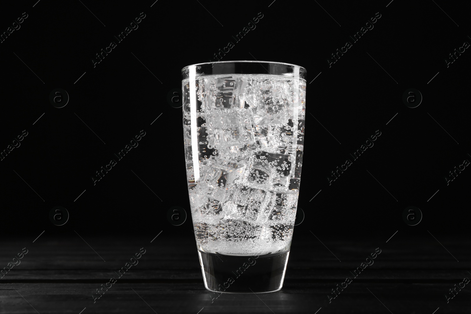 Photo of Refreshing soda water with ice cubes in glass on black wooden table