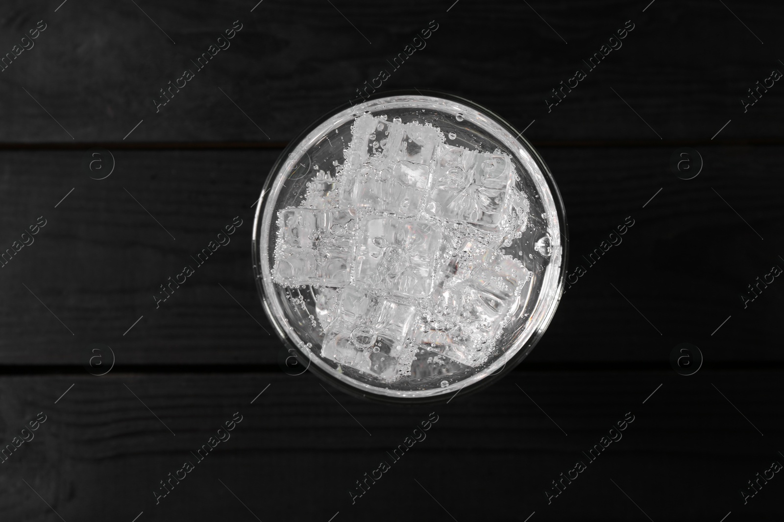 Photo of Refreshing soda water with ice cubes in glass on black wooden table, top view