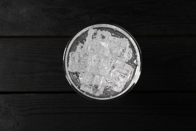 Photo of Refreshing soda water with ice cubes in glass on black wooden table, top view