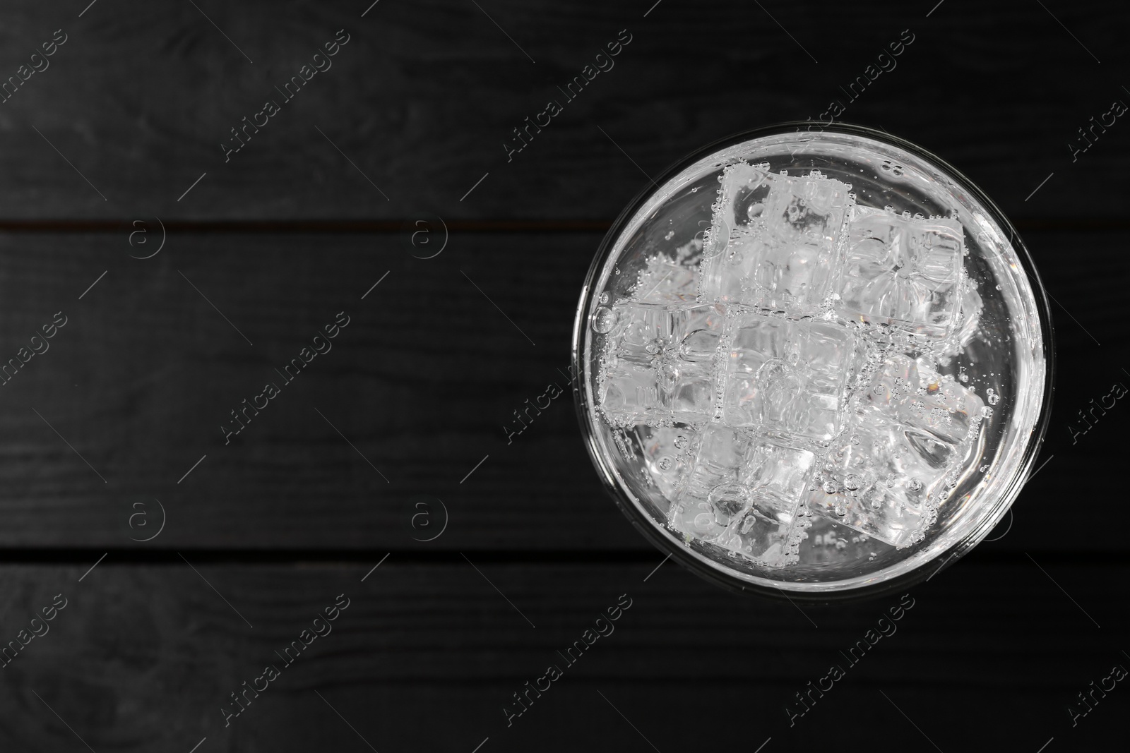 Photo of Refreshing soda water with ice cubes in glass on black wooden table, top view. Space for text