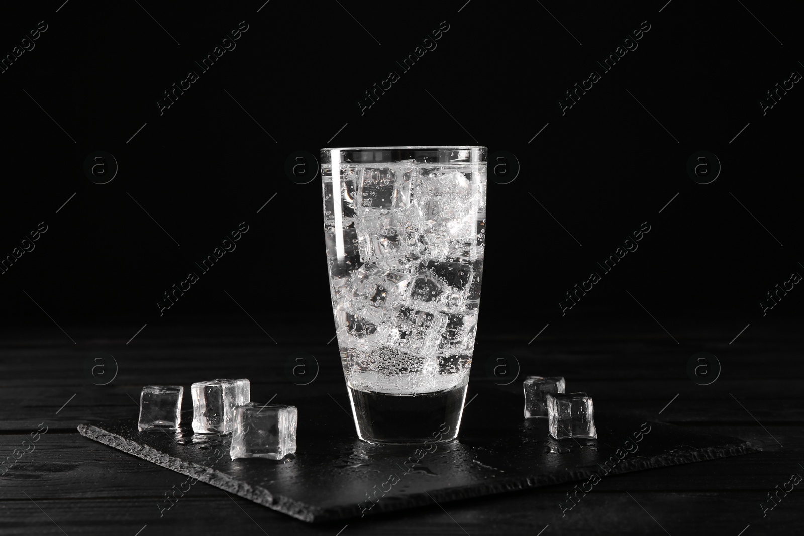 Photo of Refreshing soda water in glass with ice cubes on black wooden table