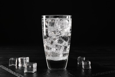 Photo of Refreshing soda water in glass with ice cubes on black wooden table