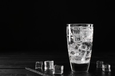 Photo of Refreshing soda water in glass with ice cubes on black wooden table, space for text