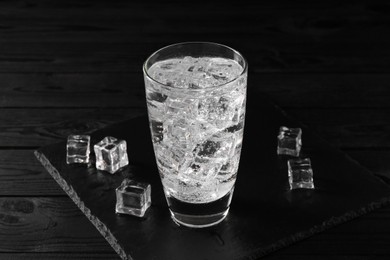 Photo of Refreshing soda water in glass with ice cubes on black wooden table