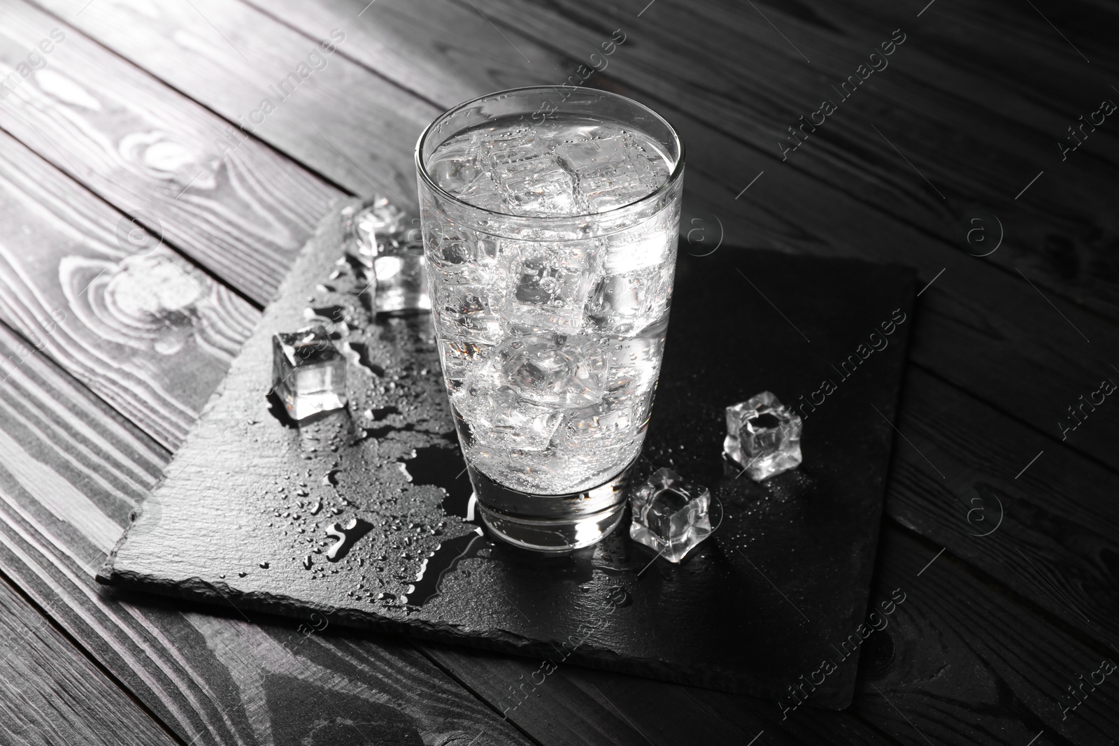 Photo of Refreshing soda water in glass with ice cubes on black wooden table