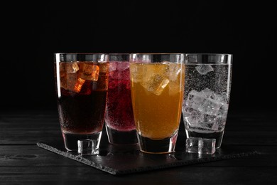 Photo of Refreshing soda water of different flavors with ice cubes in glasses on black wooden table