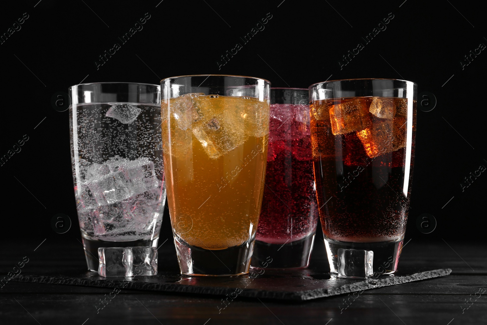 Photo of Refreshing soda water of different flavors with ice cubes in glasses on black wooden table