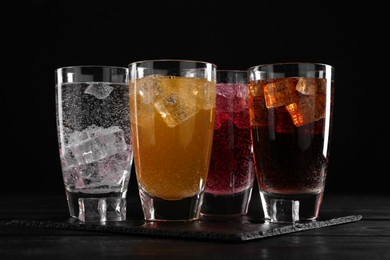 Photo of Refreshing soda water of different flavors with ice cubes in glasses on black wooden table