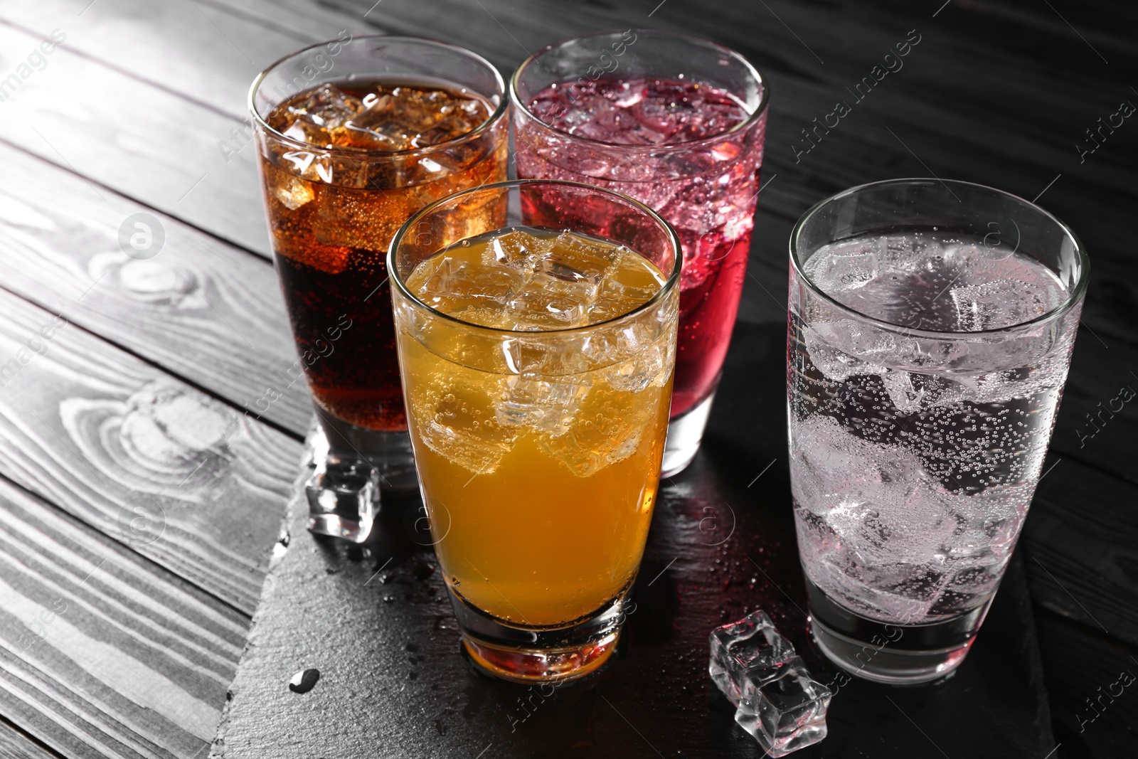 Photo of Refreshing soda water of different flavors with ice cubes in glasses on black wooden table