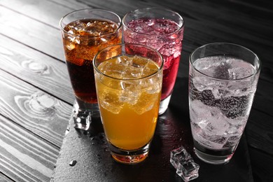 Photo of Refreshing soda water of different flavors with ice cubes in glasses on black wooden table