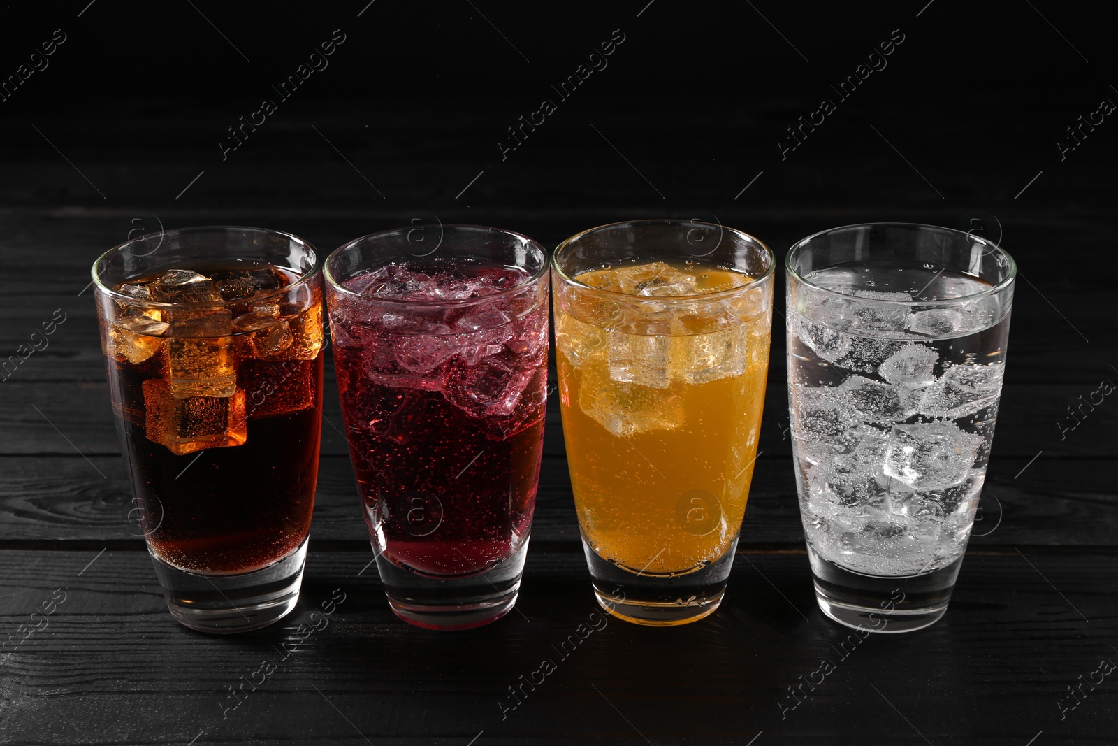 Photo of Refreshing soda water of different flavors with ice cubes in glasses on black wooden table