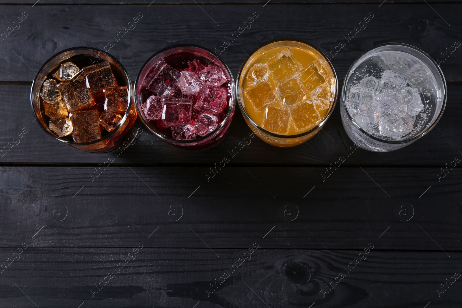 Photo of Refreshing soda water of different flavors with ice cubes in glasses on black wooden table, flat lay. Space for text