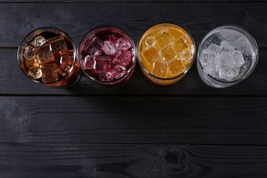 Photo of Refreshing soda water of different flavors with ice cubes in glasses on black wooden table, flat lay. Space for text