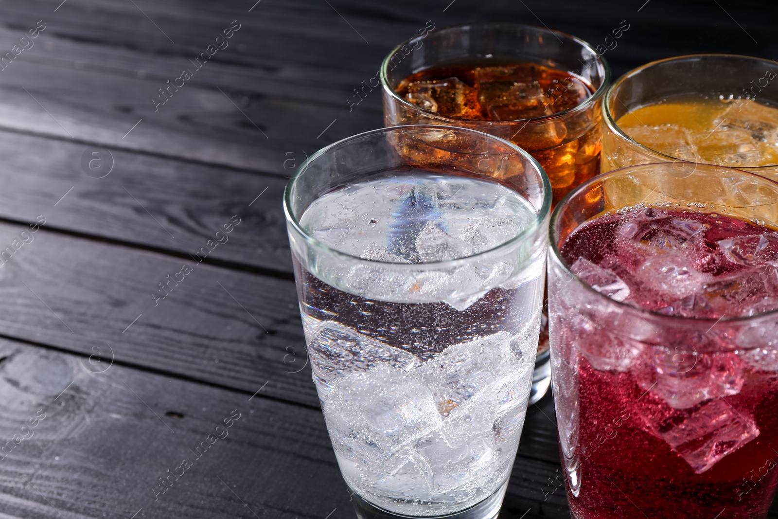 Photo of Refreshing soda water of different flavors with ice cubes in glasses on black wooden table, closeup. Space for text