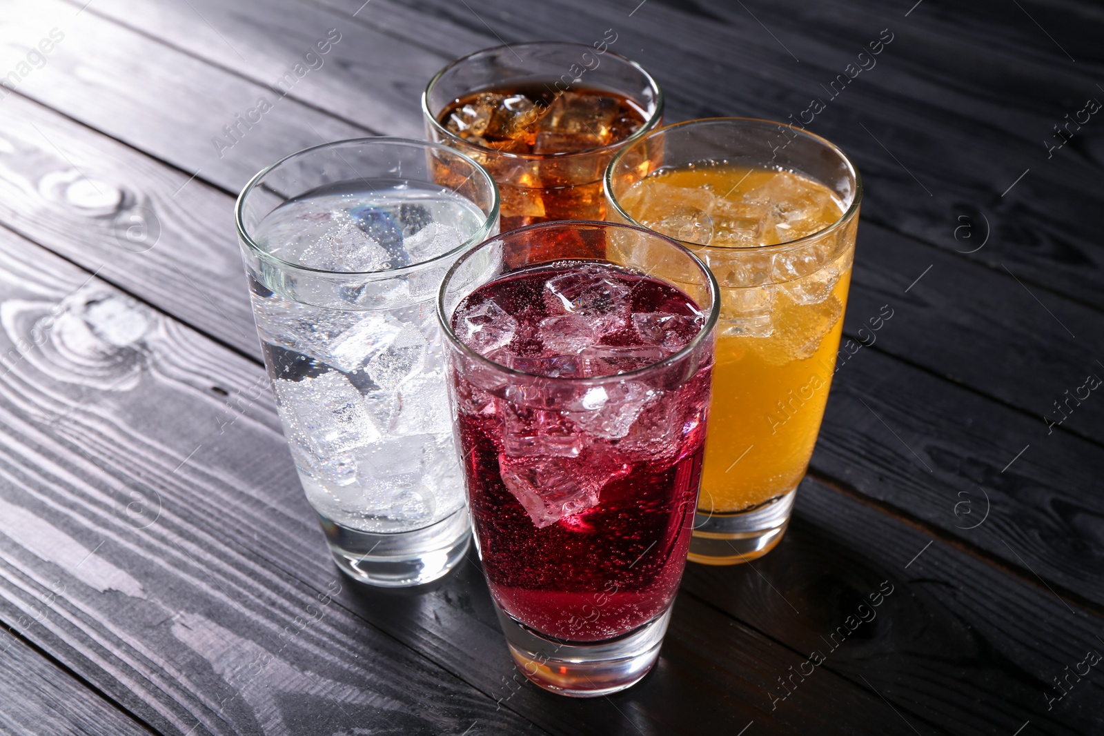 Photo of Refreshing soda water of different flavors with ice cubes in glasses on black wooden table