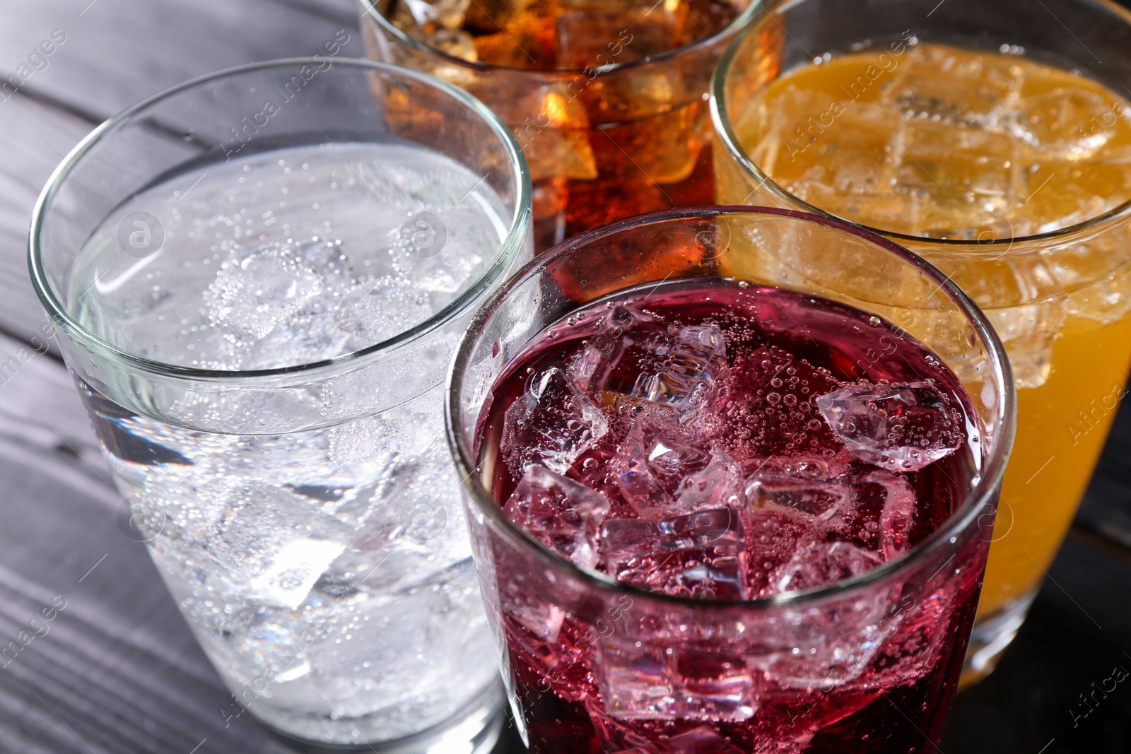 Photo of Refreshing soda water of different flavors with ice cubes in glasses on table, closeup