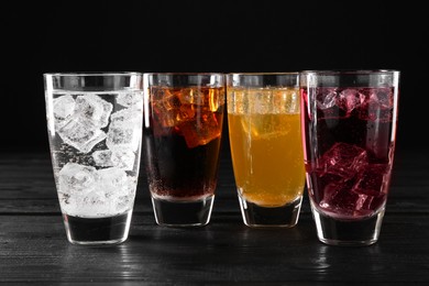 Photo of Refreshing soda water of different flavors with ice cubes in glasses on black wooden table