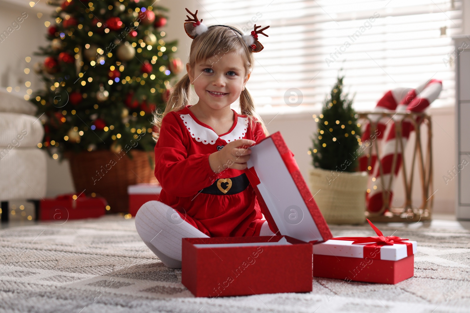 Photo of Little girl in Christmas costume with gift boxes at home