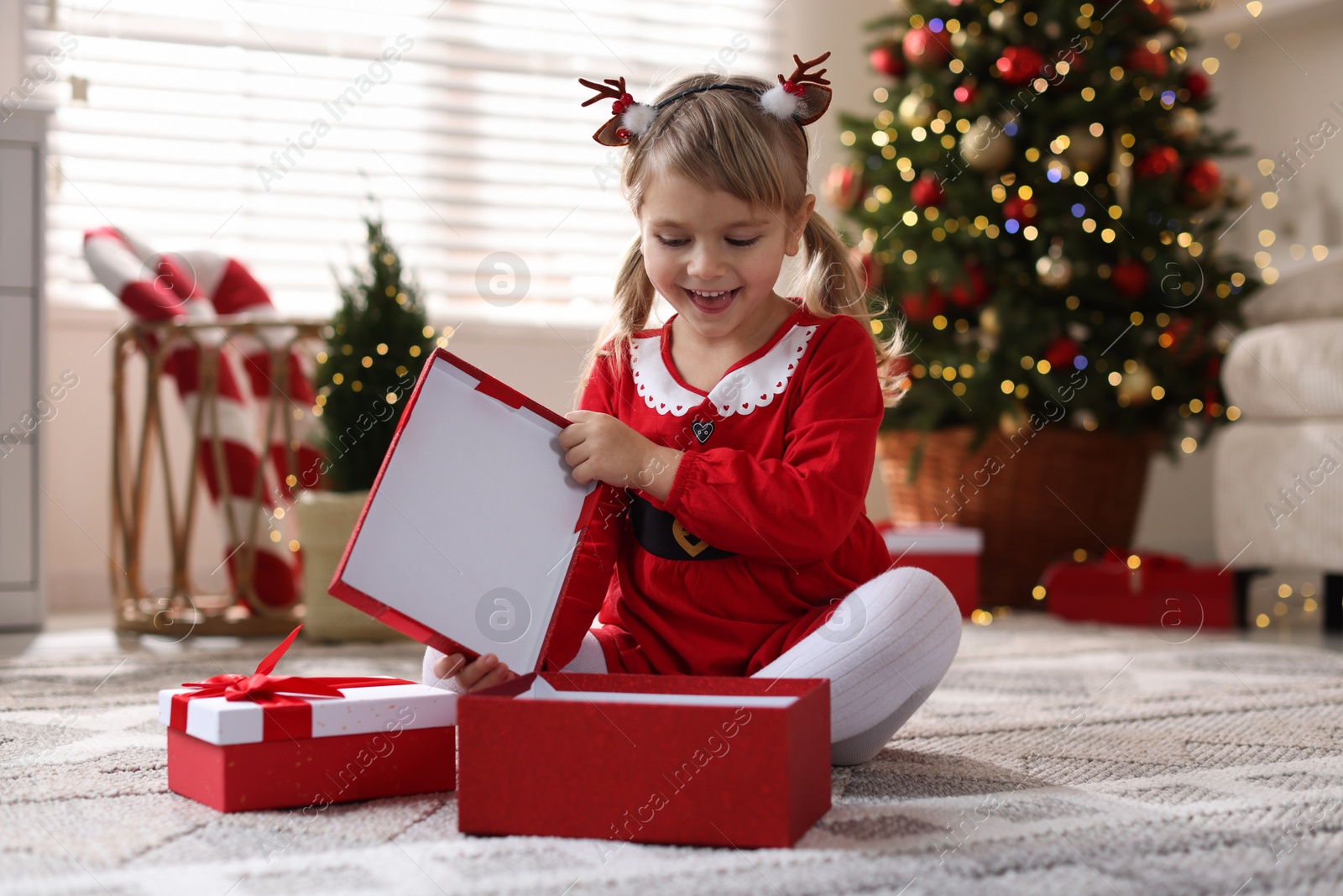 Photo of Little girl in Christmas costume with gift boxes at home