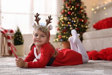 Photo of Little girl in Christmas costume with candy cane lying on floor at home