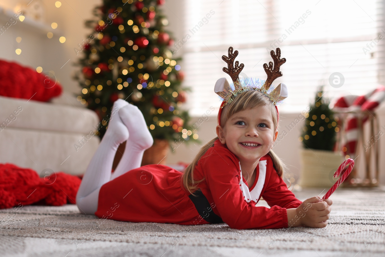 Photo of Little girl in Christmas costume with candy cane lying on floor at home