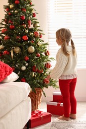 Photo of Little girl near decorated Christmas tree at home, back view