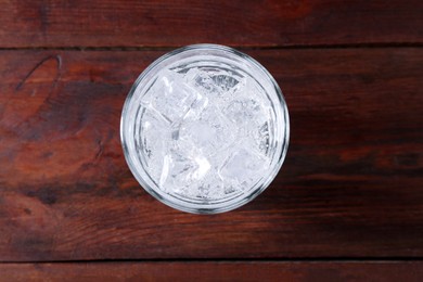 Photo of Refreshing soda water with ice cubes in glass on wooden table, top view