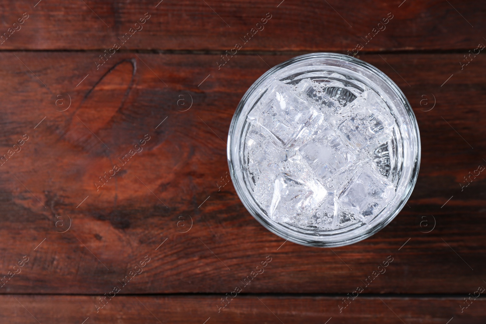 Photo of Refreshing soda water with ice cubes in glass on wooden table, top view. Space for text