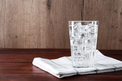 Photo of Refreshing soda water with ice cubes in glass on wooden table, space for text