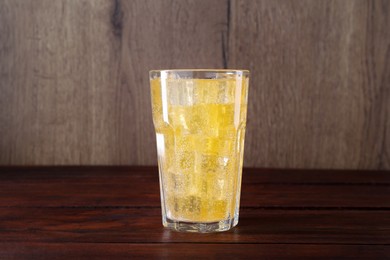 Photo of Sweet soda water with ice cubes in glass on wooden table